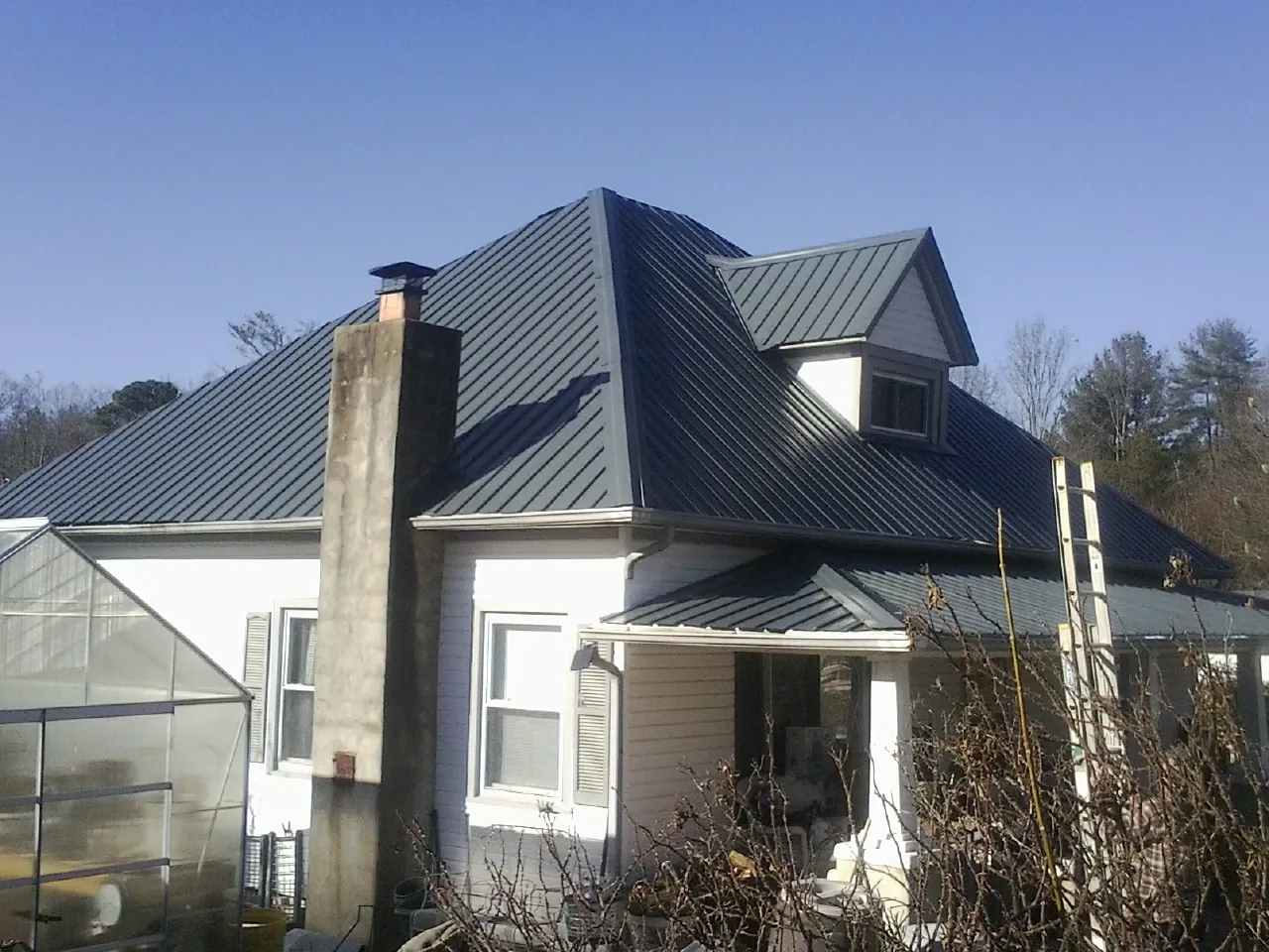 Dark blue standing seam metal roof on a white farmhouse with dormer — Slate & Tile Roof Repair by Roofing Brothers in Bells