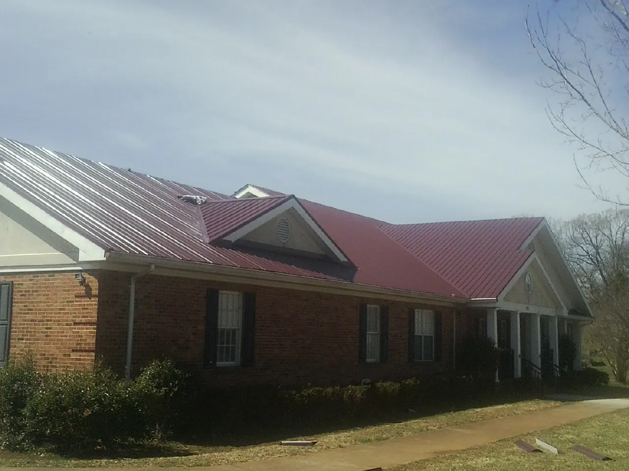 Red metal roof with gabled entries on a long brick building, from a Hail Damage Roof Repair job in Bells