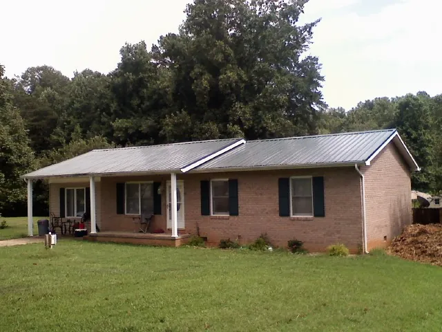 Gray metal roof on a brick ranch house with a side carport in Bells