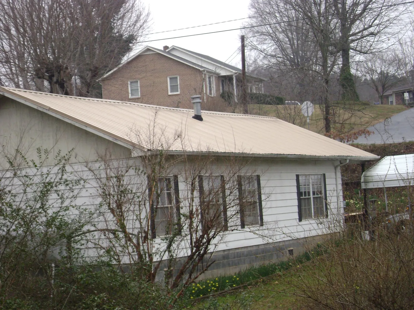 Tan metal roof on a white sided house set into a hillside — Commercial Roofing by Roofing Brothers in Bells